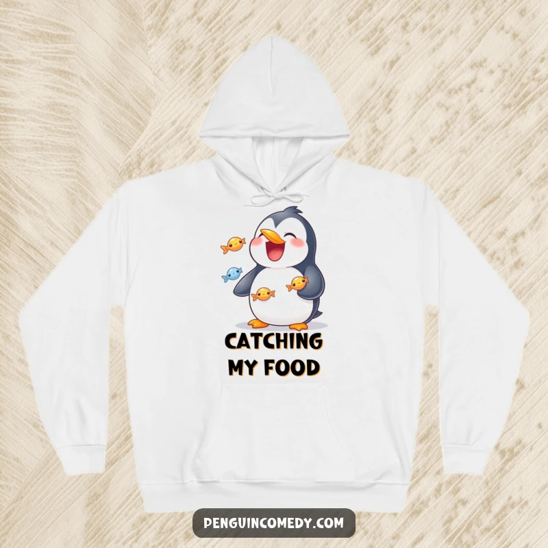 Funny hoodie with a penguin sporting a wide smile, juggling multiple shiny fish with impressive flipper dexterity.