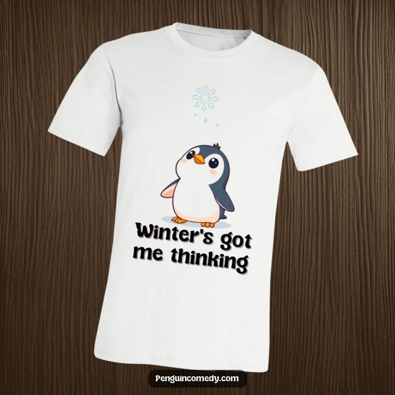 Funny T-Shirt: A curious penguin character gazing upwards at a delicate falling snowflake, full of wonder.